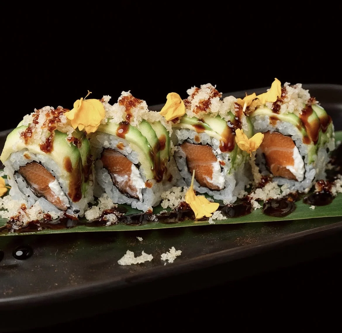 Roll di salmone e avocado con riso croccante e petali, su foglia di banano
